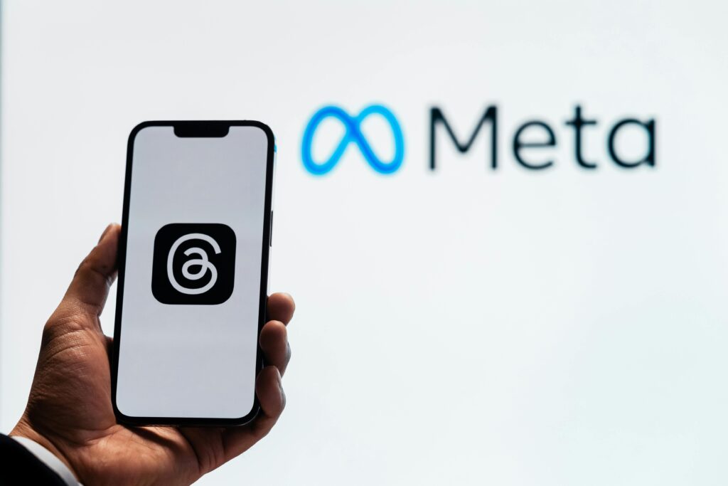 pexels-photo-17614476-17614476 A hand holding a smartphone showing the Threads app with Meta logo in the background.